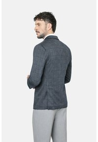 Blazer de cuadros marino hecho de tejido texturizado con cierre de dos botones, solapas de muesca y aberturas laterales, combinado con pantalones gris claro.