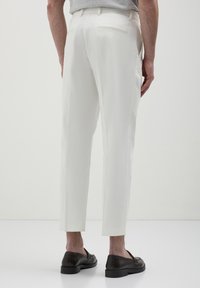 Pantaloni bianchi con una vestibilità sartoriale, dotati di linee eleganti, tasca piatta e due tasche posteriori, abbinati a mocassini scuri per un contrasto.