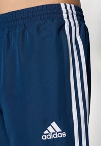 Calções atléticos azul marinho feitos de um tecido suave, com três riscas brancas laterais e um logotipo da Adidas bordado em branco.