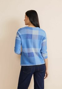 Helles blaugemustertes Sweatshirt mit langen Ärmeln, weichem Material und lockerer Passform. Es zeigt verschiedene Blautöne in einem Karomuster.