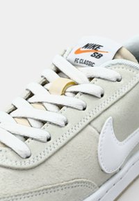 Baskets Nike SB FC Classic en daim beige clair avec lacets blancs et finition texturée. Caractéristiques d'un logo blanc et d'accents crème.