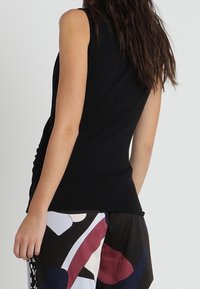 Top nero senza maniche con un design aderente, caratterizzato da una texture arricciata sul lato, abbinato a pantaloni corti larghi con motivo.