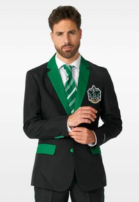 Schwarzer Blazer mit grünen Revers und Taschenbesatz. Mit einem Hauswappen auf der linken Seite, ergänzt durch eine grün-weiß gestreifte Krawatte.