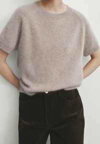 Pull léger beige clair à manches courtes fabriqué dans un matériau doux et duveteux, associé à un pantalon en velours côtelé marron foncé avec un bouton et des poches latérales.