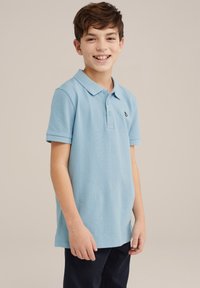 Gaiši zilā polo krekls no teksturēta auduma, ar trīs pogām un nelielu melnu logo kreisajā krūtī.