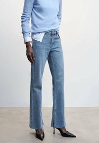 Jeans bleu clair avec une coupe droite, ourlet déchiré et décoloration subtile. Associés à un pull bleu clair et des escarpins noirs à bout pointu.