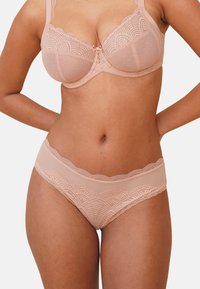 Lace-trimmed balconette bra and matching thong in nude. Bra features polka dot and scalloped designs; soft mesh with intricate patterns.