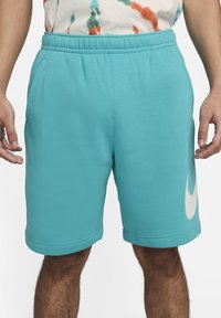 Shorts Nike en color turquesa con cinturilla elástica, bolsillos laterales y un gran logo blanco en el muslo derecho. Textura de tela suave.