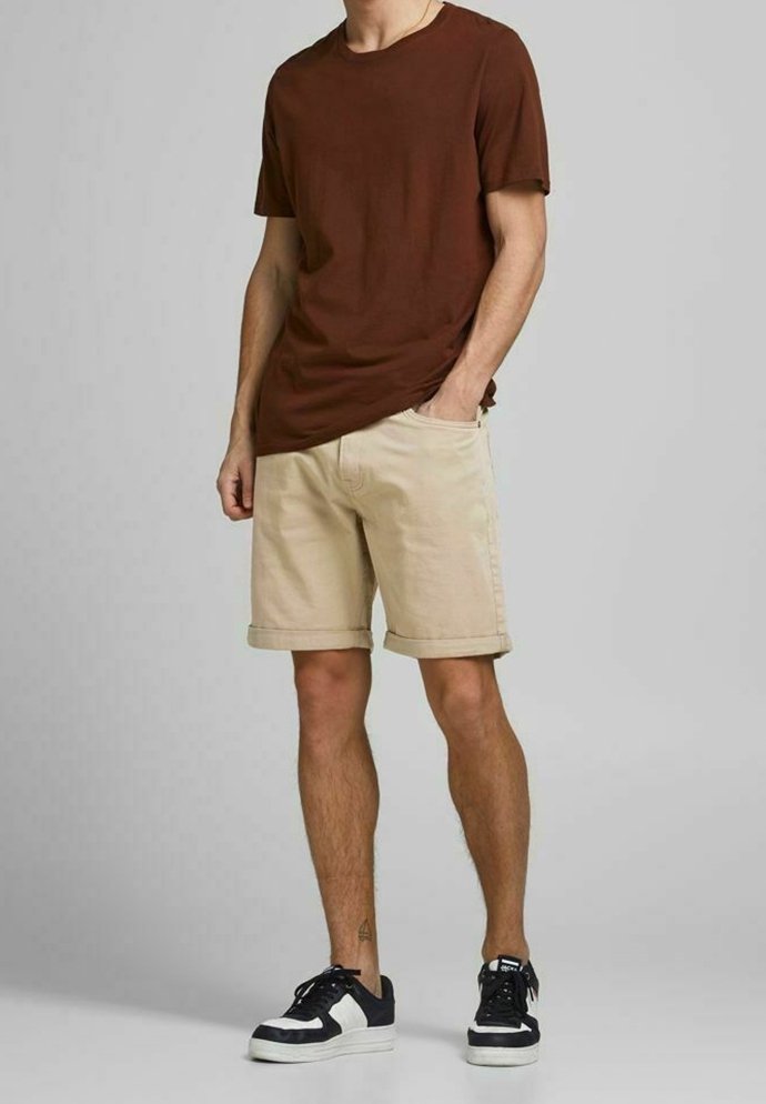 Camiseta marrón de cuello redondo, pantalones cortos beige claros y zapatillas negras con detalles blancos. Ajuste casual con dobladillo enrollado en los pantalones cortos.