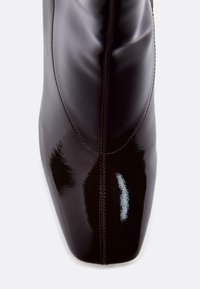 Kiiltävä musta nahkasaapas, jossa on terävä kärki, elegantti ompelu sivuilla ja sileä, kiillotettu pinta.