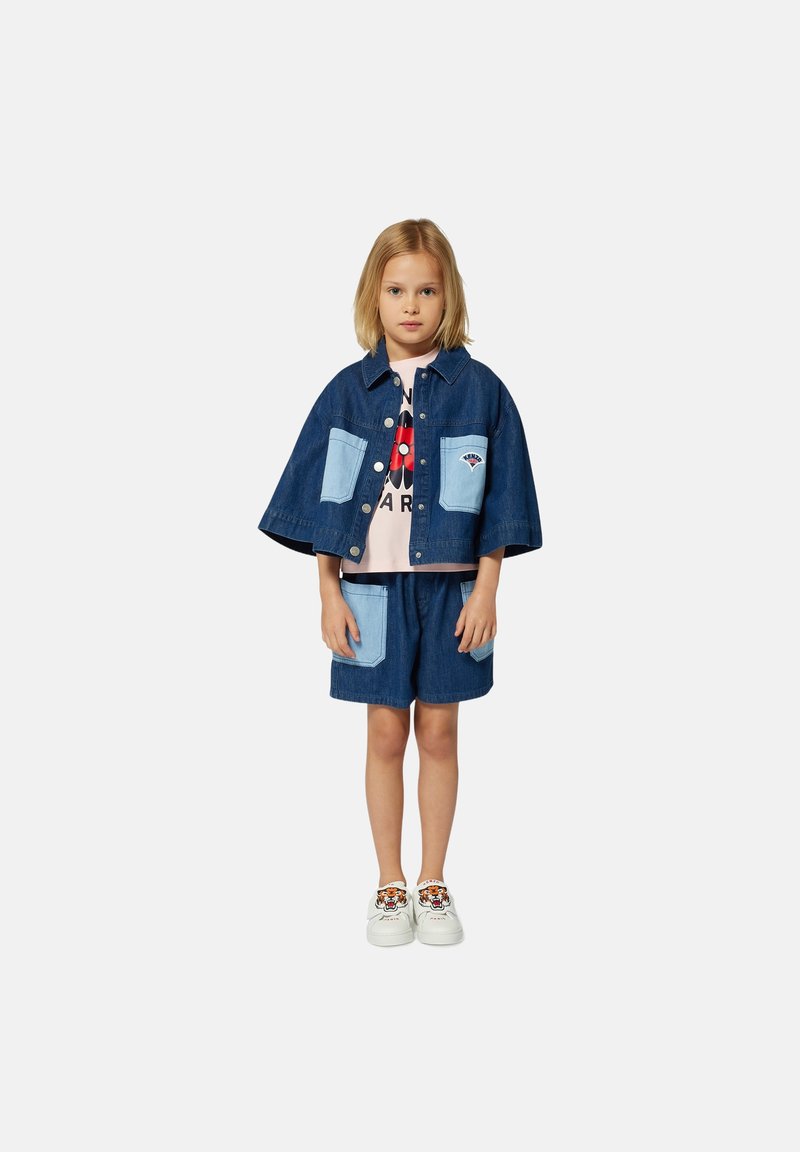 Denim jacket with short sleeves, light blue pockets, and snap buttons. Paired with denim shorts featuring matching pockets. White sneakers with tiger design.