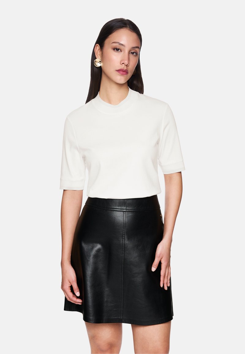 Weißes kurzärmliges Oberteil mit hohem Kragen, kombiniert mit einem schwarzen Leder-A-Linien-Rock, der eine glatte Textur und einen passenden Taillenbund aufweist.