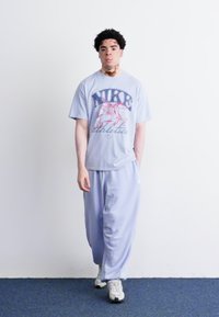 Lyseblåt Nike grafisk t-shirt med et pink og rødt logo, parret med matchende lysblå løstsiddende bukser og hvide sneakers.
