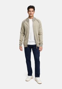 Lichtgrijze gebreide cardigan met een rits aan de voorkant, geribbelde manchetten en textuurdetails op de schouders, gecombineerd met donkere jeans en witte sneakers.