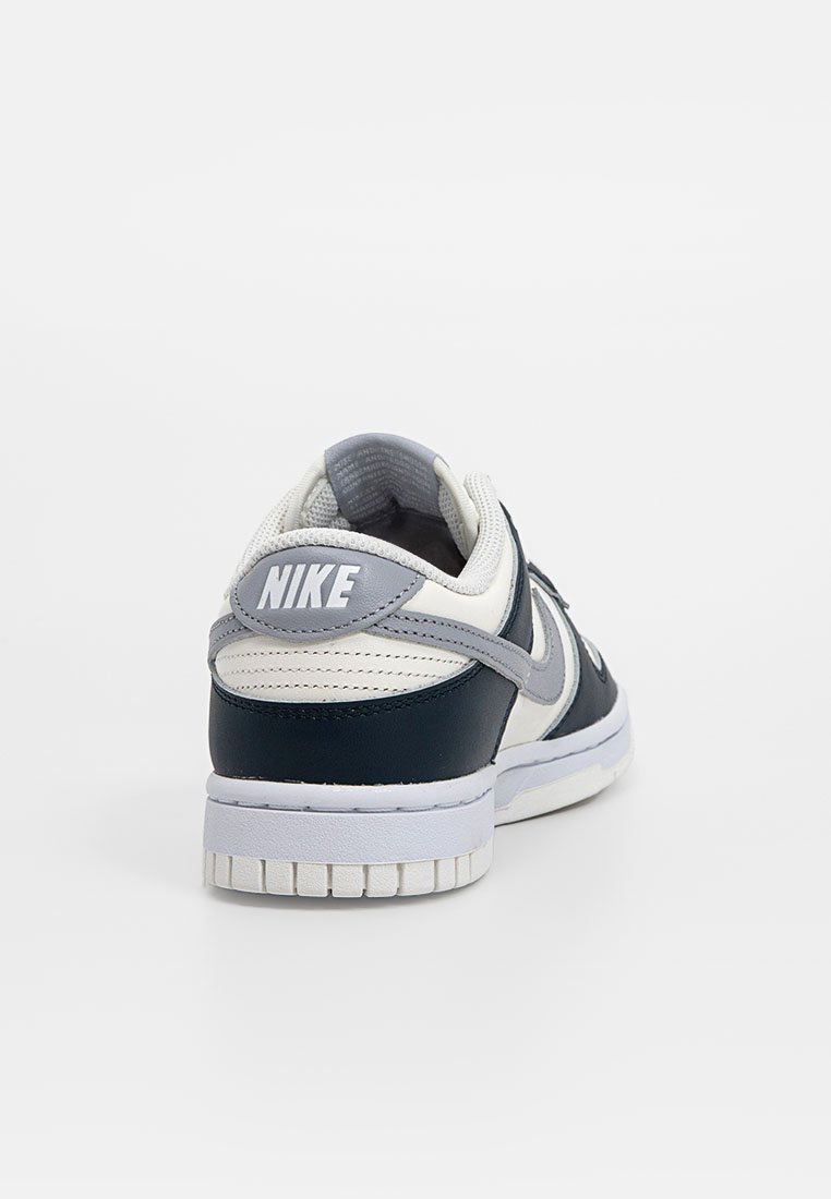 Sneakers Nike con tomaia in pelle blu navy e tessuto bianco, caratterizzati da uno swoosh grigio, collare imbottito e suola in gomma con battistrada testurizzato.