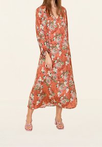 Maxikjol i rostorange med blommönster, långa ärmar, V-ringning och flödande silhuett. Matchas med rosa klacksandaler.