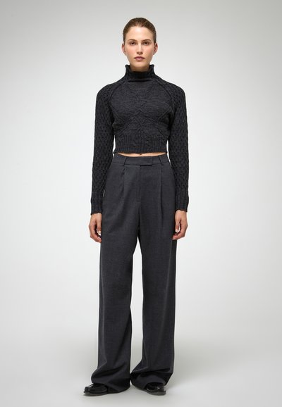 Zwarte, gebreide, coltrui crop top met een gestructureerd patroon, gecombineerd met hoge, wijdvallende, donkergrijze broek met plooien aan de voorkant.