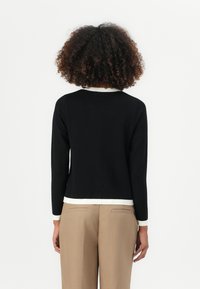 Svart langermet topp med rund hals og kontrastfarget hvit kanting nederst og på ermene, sammen med beige skræddersydde bukser.