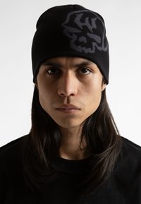 Bonnet en tricot noir avec un design graphique gris. Tissu texturé qui s'adapte parfaitement, complétant la silhouette globale simple et fonctionnelle.