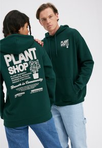Green hooded sweatshirt featuring a white graphic print on the back, including plants and text. Front has a smaller logo. Casual fit.