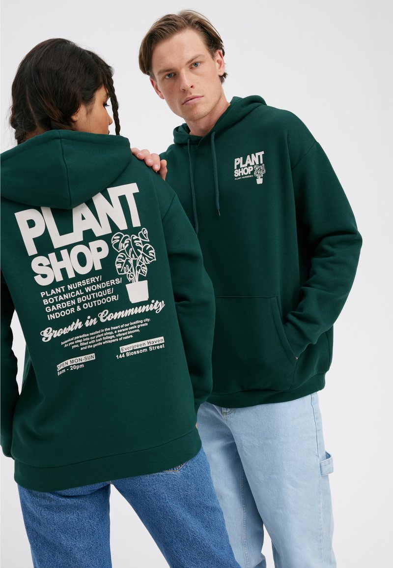 Green hooded sweatshirt featuring a white graphic print on the back, including plants and text. Front has a smaller logo. Casual fit.