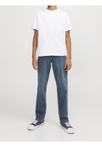 Persona vistiendo una camiseta blanca de manga corta, jeans azules y zapatillas azul marino con suelas y cordones blancos.