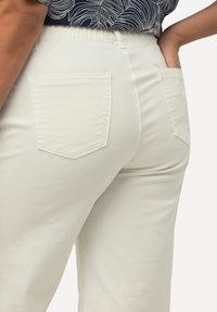 Pantalones de mezcla de algodón blancos con cintura alta y banda elástica. Cuenta con dos bolsillos traseros con detalles de costura. Textura suave.