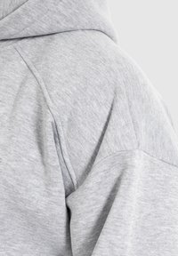 Grauer Hoodie mit einem strukturierten, weichen Stoff und lockerer Passform. Das Design umfasst eine Kapuze und sichtbare Nähdetails an den Nähten.