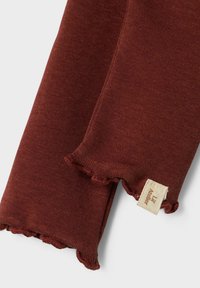 Rustfarbener, gerippter Stoff mit gewelltem Rand und einem kleinen beigen Schild mit der Aufschrift "Lil Atelier." Weicher Stoff mit einer engen Passform.