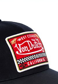 Crna kapa s crvenim izvezenim grbom "West Coast Von Dutch" te kariranim uzorkom. Grb ima zlatne detalje i bijele rubove.