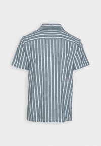 Košile s krátkým rukávem a límečkem v modro-bílé vertikální pruhované vzoru. Vyrobena z texturované látky s čistým zakončením na spodním okraji a rukávech.