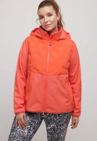 Světlá oranžová bunda s kapucí, s prošívanou horní částí a hladkou dolní částí. V kombinaci s černobílými legínami s vzorem.