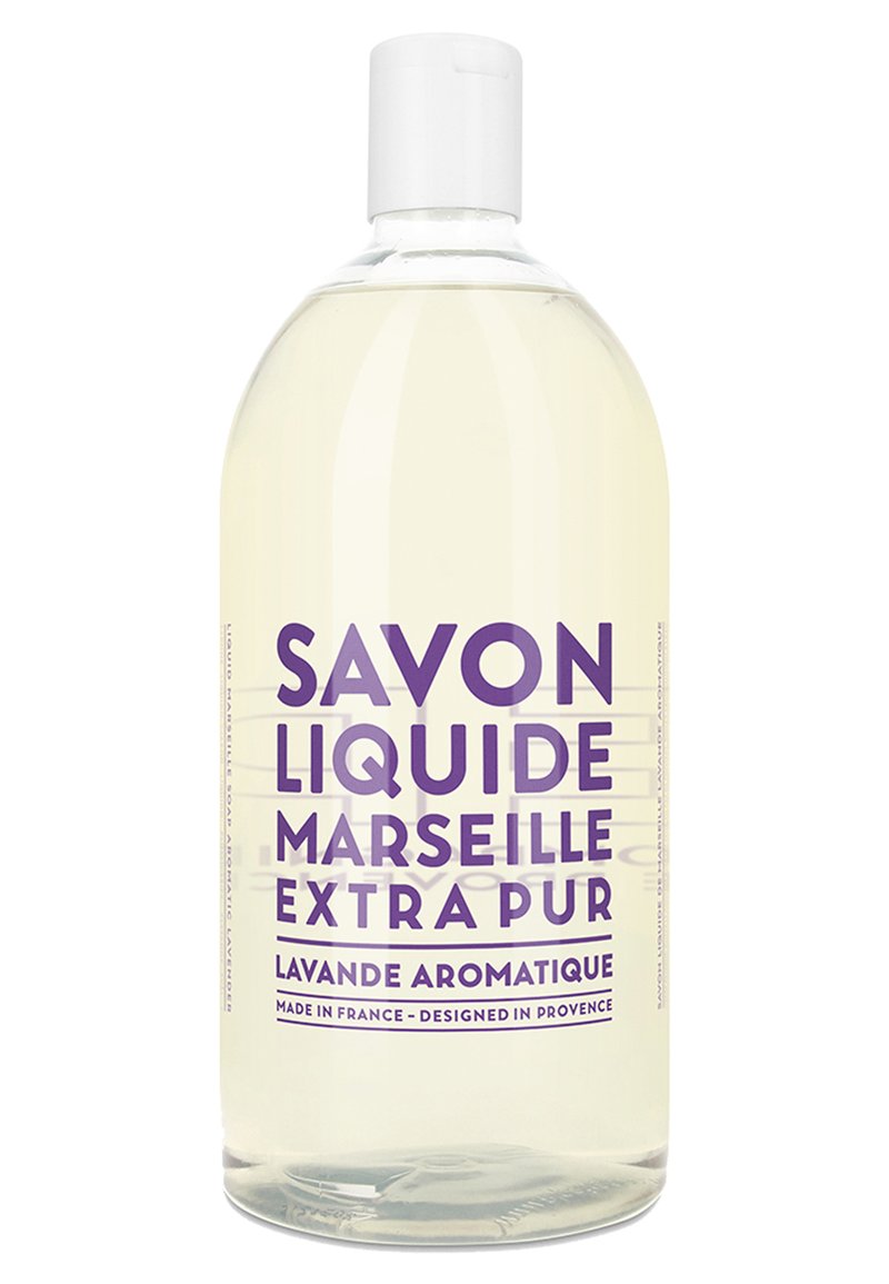 Sapone liquido trasparente in una bottiglia trasparente. Cappuccio bianco, testo in grassetto di colore viola: "SAPONE LIQUIDO DI MARSEIGNE EXTRA PURO AROMA DI LAVANDA."