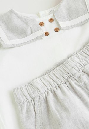 Biały top z szarym kołnierzykiem ozdobiony trzema brązowymi guzikami, w połączeniu z szarym dołem z elastycznym pasem, wykonany z lekkiego materiału.