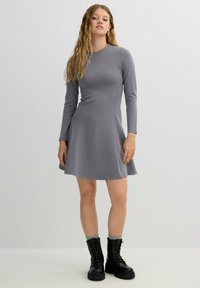 Vestido gris de manga larga con falda acampanada. Tejido liso y elástico con escote redondo. Combinado con botas negras con cordones y calcetines grises.