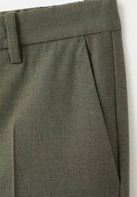 Gros plan sur la ceinture et le détail de la poche en biais d'un pantalon en tissu texturé vert olive.