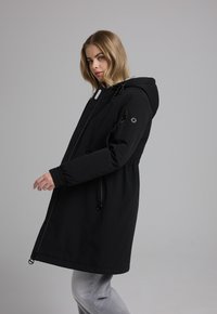 Zwarte waterdichte parka met een capuchon, voorzien van ritszakken, elastische mouwen en een verstelbare taillekoord voor een veilige pasvorm.