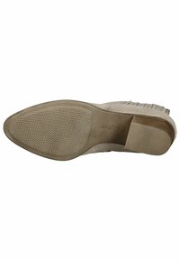 Botín beige hasta el tobillo con un acabado de ante liso, suela de goma plana y patrón texturizado. Presenta un detalle de flecos en el costado.