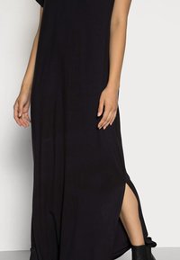 Svart maxiklänning med korta ärmar, sidoklyftor och slät textur. Bärs med svart boots som går till anklarna. Enkel, rak skärning.