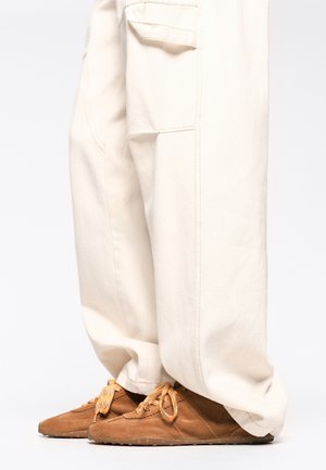 Pantaloni cargo beige dalla vestibilità ampia con tasche laterali; abbinati a scarpe in suede marroni con lacci arancioni e suole in gomma.