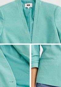 Blazer turquesa hecho de una tela suave, con un cuello con muescas, dos bolsillos frontales y costuras anguladas. Acentuado con un diseño simple.