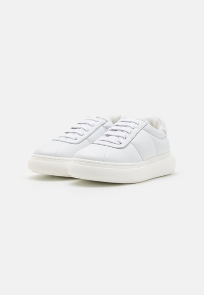 Weiße Leder-Sneaker mit glatter Textur, abgerundetem Zehenbereich, einfachem Schnürsystem und dickem weißen Gummisohle. Dezente Nahtdetails an den Seiten.