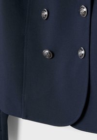 Granatowa marynarka z srebrnymi ozdobnymi guzikami z misternymi herbami, przeszywanymi krawędziami oraz lekko zaokrąglonym dołem.