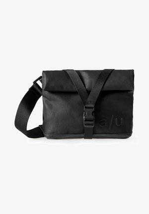 Compact black messenger bag made of durable fabric, featuring a fold-over top, adjustable strap, and embossed logo on the front.