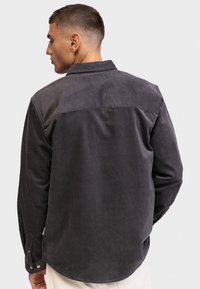 Dunkelgraues Cordhemd mit Button-Down-Kragen, langen Ärmeln und gerippter Textur. Verfügt über einen einfarbigen Rücken und verstellbare Manschetten.