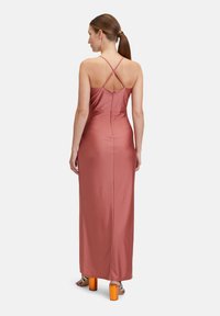 Lyserød satin maxi-kjole med krydsede stropper bagpå. Glat tekstur, tætsiddende silhuet og høj slids. Parret med orange blokhælede sandaler.