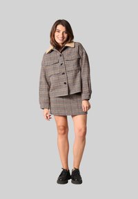 Bruin en crèmekleurige geblokte jas met een nepbont kraag, gecombineerd met een bijpassende geblokte mini-jurk en gedragen met zwarte schoenen.