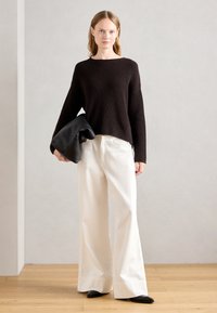 Maglione nero a righe con maniche ampie, abbinato a pantaloni ampi color avorio. Il modello tiene una borsa in pelle nera, con scarpe nere a punta visibili.