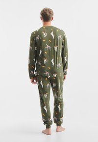 Zelený pyžamový komplet s ilustracemi psů a různobarevnými akcenty a vzory. Dlouhé rukávy a elastické manžety na kalhotách.