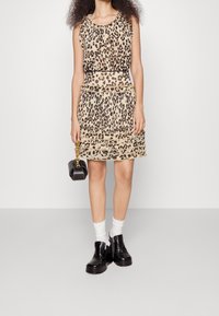 Robe à imprimé léopard avec des volants superposés, en beige et noir, assortie à des chaussures noires épaisses et des chaussettes blanches à la cheville. Sac à main noir.